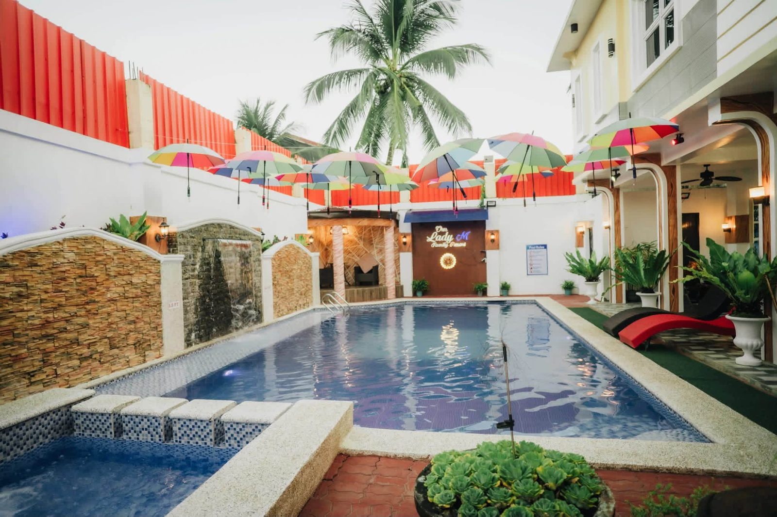 Courtyard pool with colorful umbrellas hanging overhead and a palm tree behind the cabana