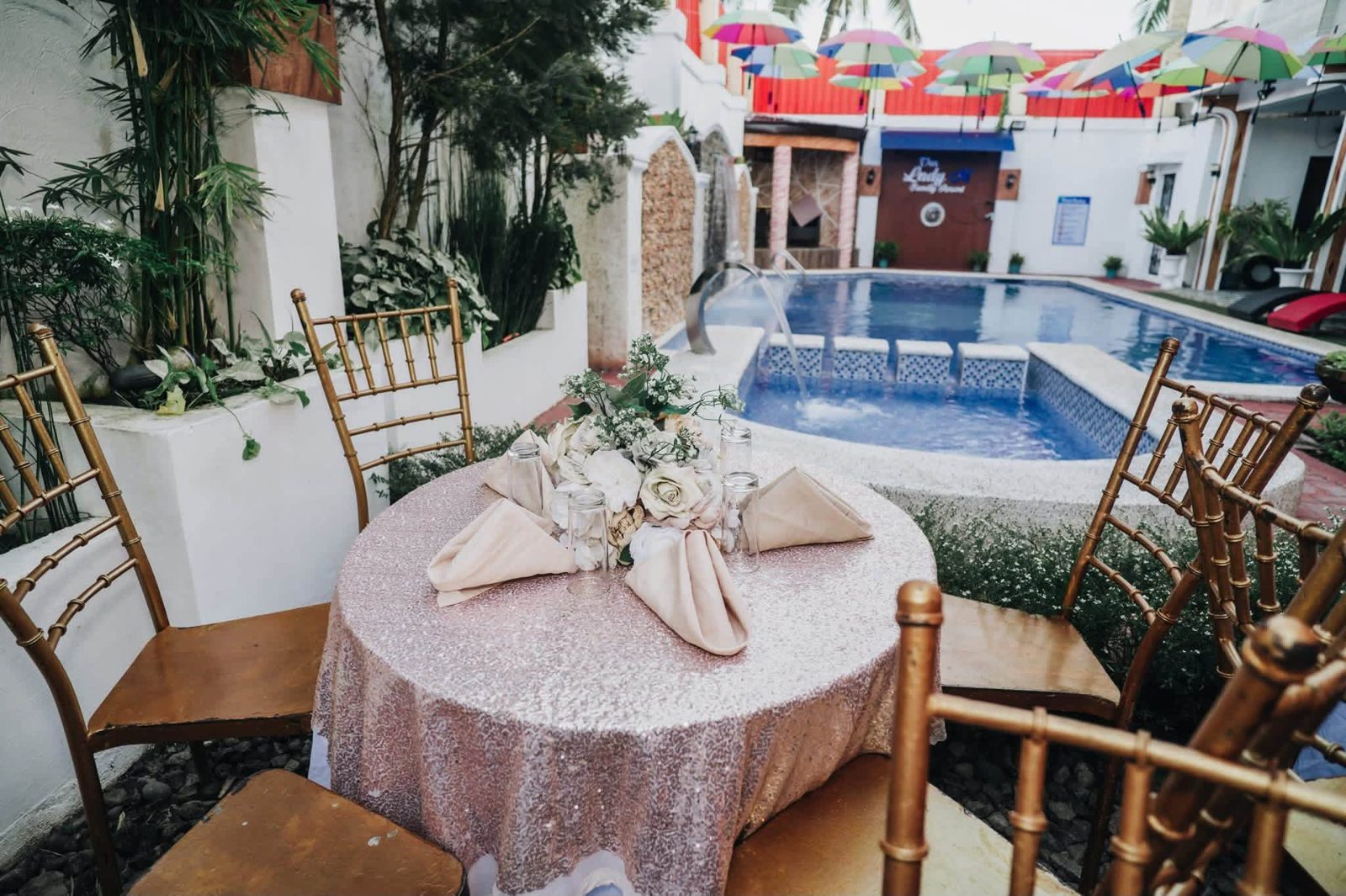 Round table with sequin cloth and white roses, gold chairs, and the pool behind